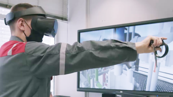 trainee tests the Chemical Technician training in VR. The TV in the background mirrors what they see.